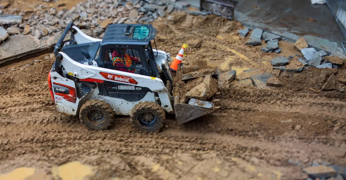 A skid steer loader moves rocks on a muddy construction site, showcasing construction machinery in action.