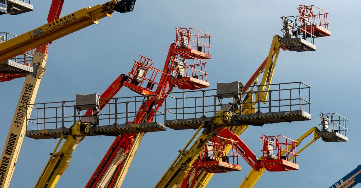 pexels-photo-32114503-32114503 Vibrant boom lifts reaching skyward, showcasing industrial machinery against a clear blue backdrop.