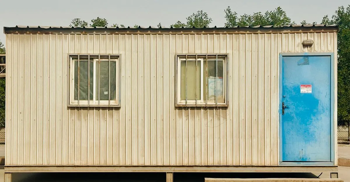 pexels-photo-35385946-35385946 A portable cabin with a distinctive blue door in a sunny outdoor setting in Saudi Arabia.