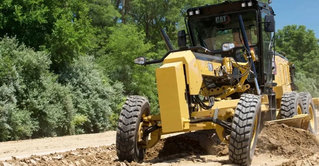 pexels-photo-37701411-37701411 Yellow motor grader operating at a construction site surrounded by greenery in India.