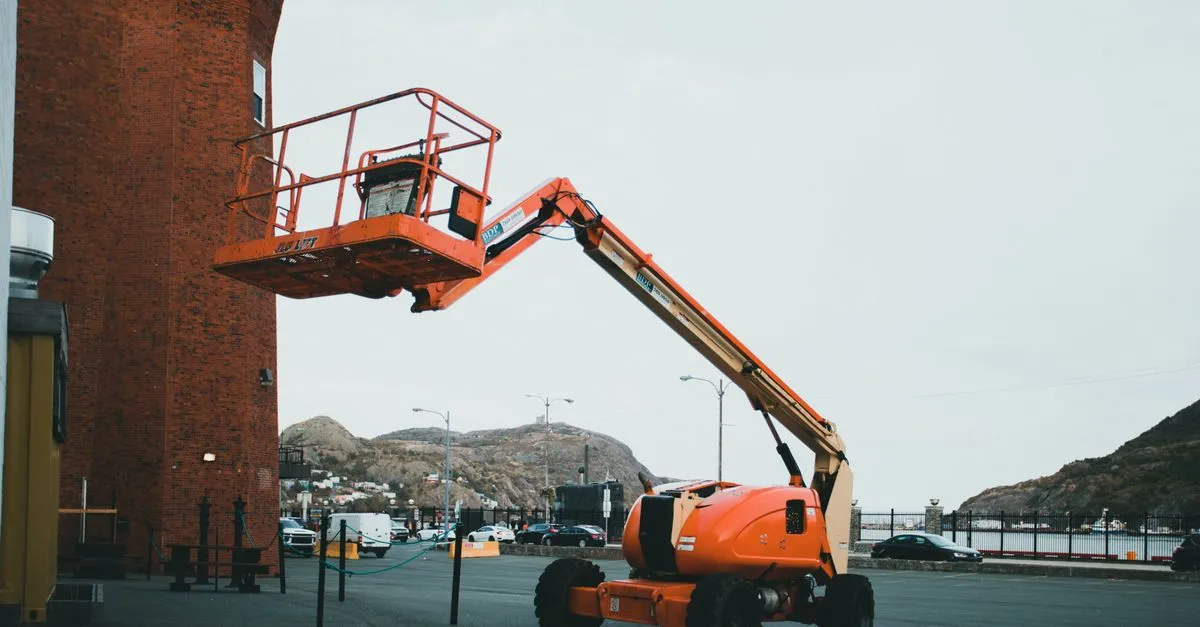An orange boom lift positioned outdoors beside a brick building in an urban setting.