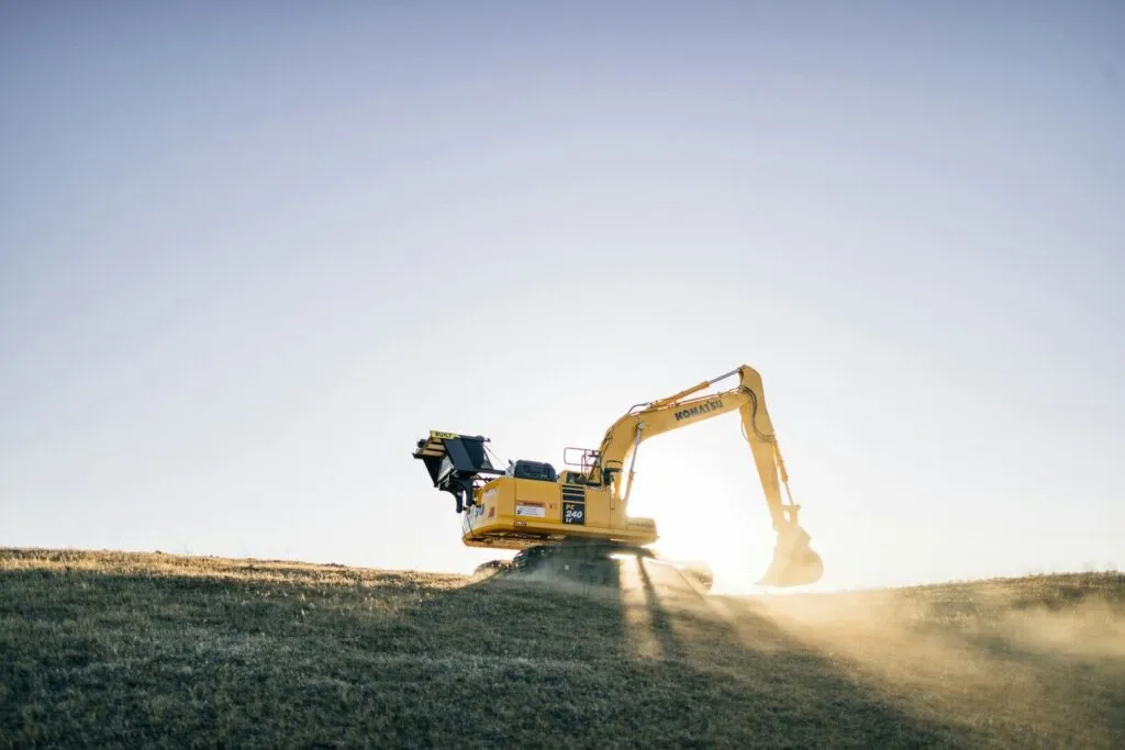 a yellow excavator on a hill with a blue sky in the background Excavator rental Abu Dhabi - chain and tyre excavator hire by Taineq UAE