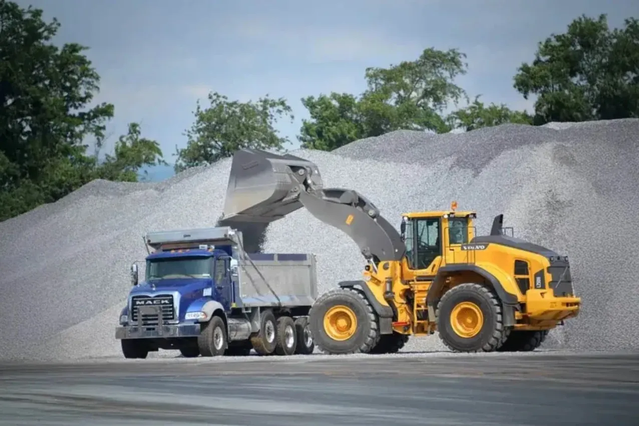 Heavy-Duty Volvo Wheel Loader Rental in Abu Dhabi – Taineq Equipment Volvo heavy-duty wheel loader loading gravel into a dump truck, available for wheel loader rental Abu Dhabi through Taineq.